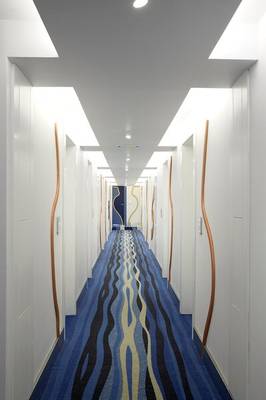 Flur im I Resort Beach Hotel & Spa mit weißen Wänden, blauen und schwarzen Teppichmustern und dekorativen Holzelementen.