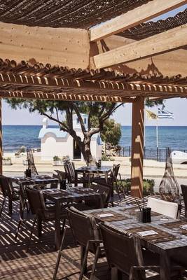 Außenbereich des Nema Design Hotels mit Tischen und Stühlen unter einem Holzdach mit Blick auf das Meer.