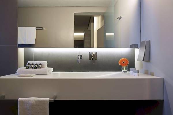 Badezimmer im Nema Design Hotel & Spa mit weißem Waschbecken, Spiegel und Handtüchern.