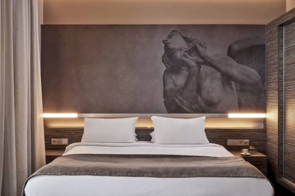 Hotelzimmer im Nema Design Hotel & Spa mit großem Wandbild, zwei weißen Kissen und gedecktem Bett.
