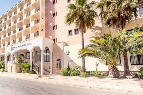 Außenansicht des La Santa Maria Playa Hotels mit Palmen und einer Straße davor.