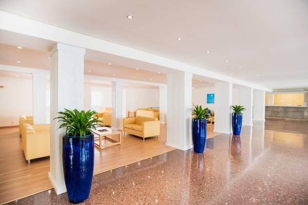 Lobby des La Santa Maria Playa Hotels mit gelben Sofas und blauen Pflanzen in großen Vasen.