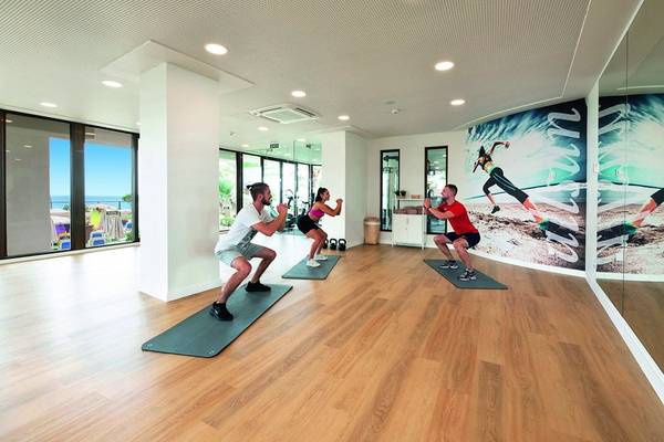 Fitnessraum im Allsun Hotel Sumba mit Personen, die auf Matten trainieren, und einer großen Wandgrafik.