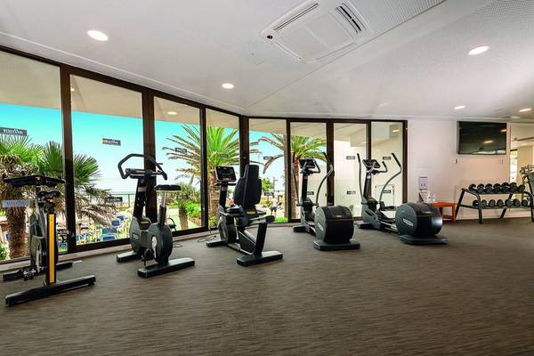 Fitnessstudio im Allsun Hotel Sumba mit Blick auf Palmen und Strand.