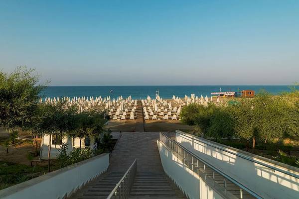 Zugang zur Strandpromenade des Sultan of Dreams Hotels mit vielen Sonnenschirmen und Bäumen.