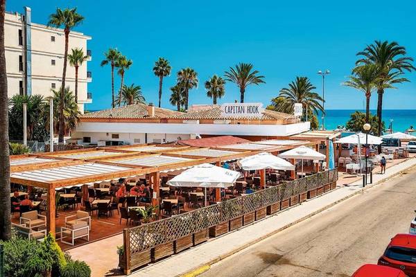 Außenterrasse des Girasol Hotel Capitan Hook mit Tischen, Stühlen und Sonnenschirmen am Meer.