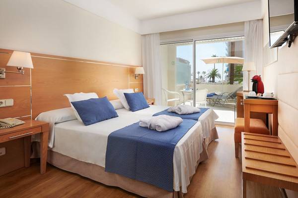 Doppelzimmer mit Balkon im Girasol Hotel, zwei Betten mit blauen Kissen, Blick auf eine Terrasse mit Möbeln.