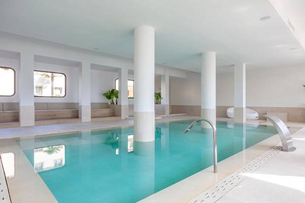 Innenpool des Aparthotel Marins Playa mit weißen Wänden und Boden, blauem Wasser und Pflanzen.