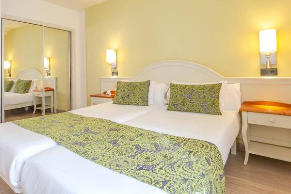 Doppelbett im Schlafzimmer des Aparthotel Marins Playa mit grünen Kissen und gelben Wänden.