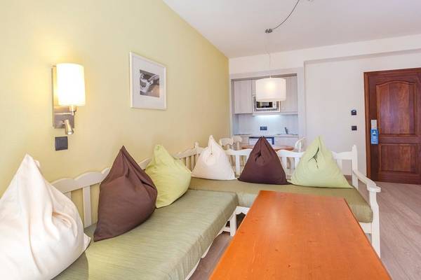 Wohnbereich im Aparthotel Marins Playa mit gelben Wänden, Möbeln und Kissen.