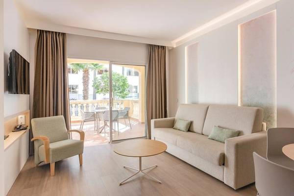 Innenbereich eines Zimmers im Aparthotel Marins Playa mit einem großen Sofa, einem Tisch und einem Balkon mit Blick auf die Außenterrasse.