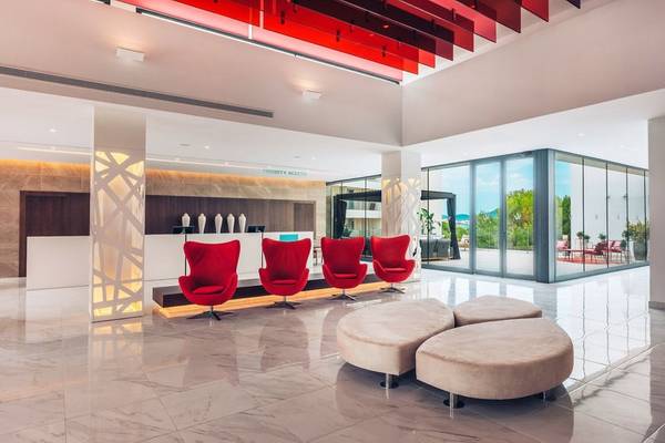 Ein modernes Hotel-Lobby mit roten Sesseln, weißen Marmorboden und großen Glastüren.