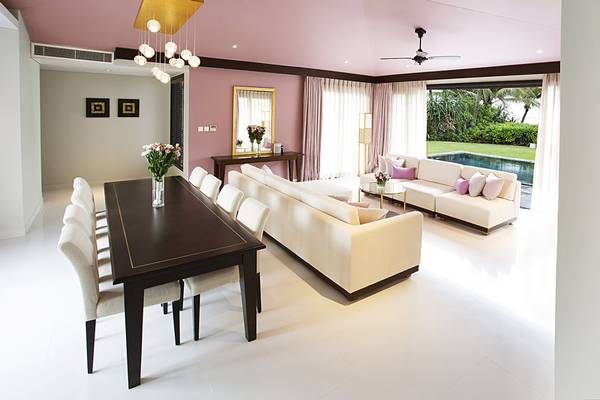 Wohnzimmer im TIA Wellness Resort mit weißem Interieur, rosa Wänden und einem großen Fenster mit Blick auf den Pool.