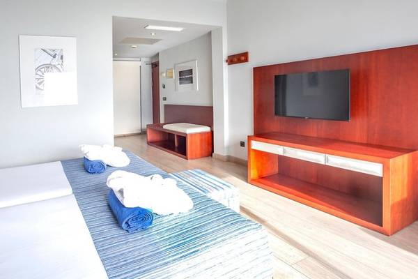 Innenansicht eines Hotelzimmers von Marins Playa Suites mit zwei Betten, Fernseher und Holzmöbeln.