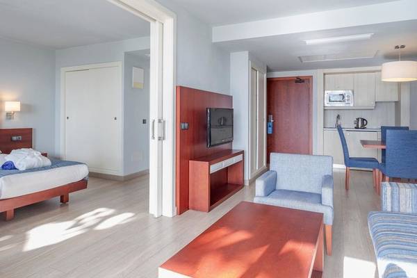 Innenansicht eines Zimmers im Marins Playa Suites Hotel mit Bett, Fernseher, Couch, Esstisch und Küchenbereich.