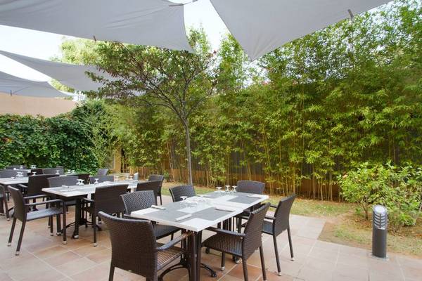 Foto von der Terrasse des Bakour Garbi Cala Millor Hotels mit Tischen und Stühle, umgeben von Bambusbepflanzung.