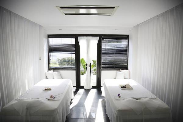 Massageraum im Tia Wellness Resort mit zwei Betten, weißen Laken, Kissen und Vorhängen.