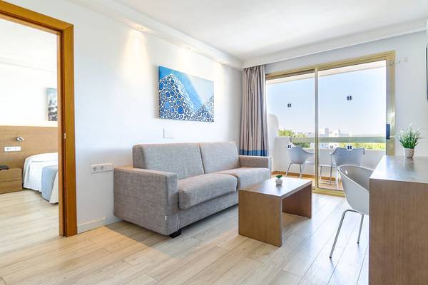 Das Wohnzimmer des Millor Sol Hotels mit grauem Sofa, Couchtisch und Fenstern.
