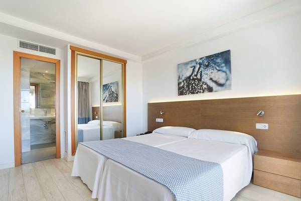 Ein modernes Hotelzimmer im Millor Sol mit einem Doppelbett, Kunstwerken an der Wand und einem Badezimmerspiegel im Hintergrund.