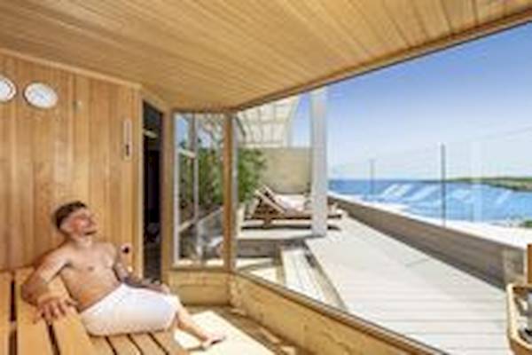 Ein Mann sitzt nackt in einer Sauna mit Aussicht auf das Meer im Allsun Hotel Borneo.