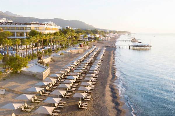 Luftaufnahme des Sherwood Exclusive Kemer Hotels mit vielen Sonnenschirmen und Liegen am Strand.