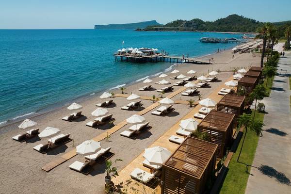 Luftaufnahme des Sherwood Exclusive Kemer Hotels mit Strand, Liegen und Sonnenschirmen.