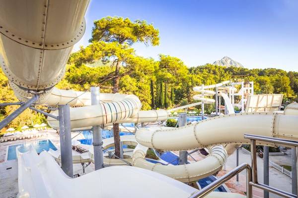 Aussicht auf die Wasserrutschen im Sherwood Exclusive Hotel Kemer mit Swimmingpool und grüner Umgebung.