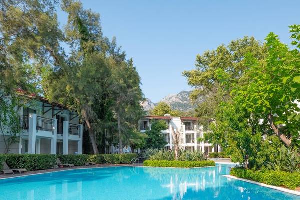 Außenbereich des Sherwood Exclusive Kemer Hotels mit Swimmingpool, Gebäuden und Bäumen.