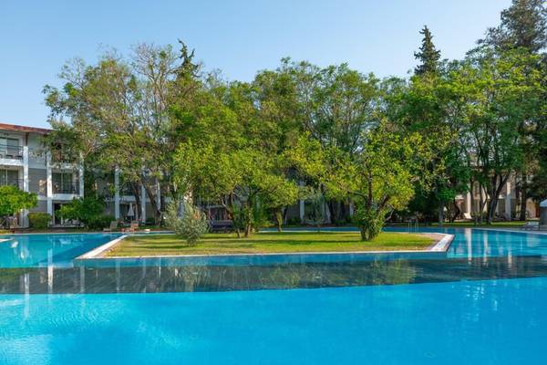 Außenpool des Sherwood Exclusive Kemer Hotels mit grünen Bäumen und Gebäude im Hintergrund