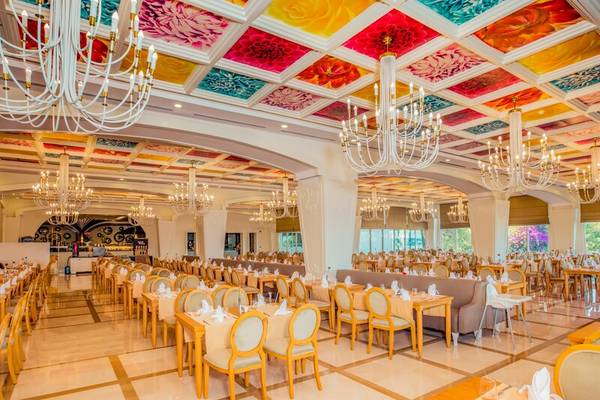 Innenansicht des Restaurants im Sherwood Exclusive Kemer Hotel mit farbenfrohen Deckengemälden und hängenden Kronleuchtern.