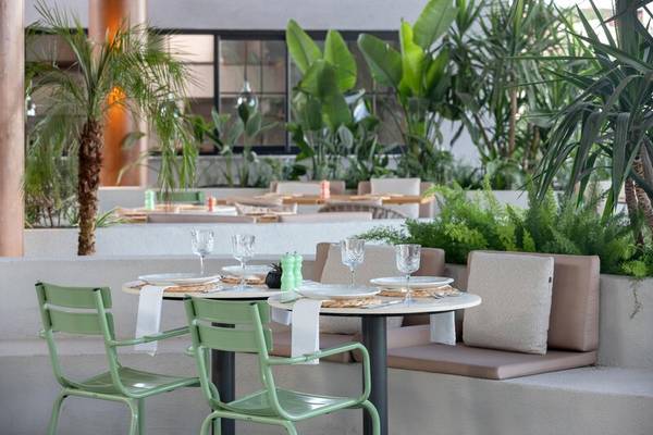 Außenbereich des Sherwood Exclusive Kemer Hotels mit grünen Stühlen und Tischen, umgeben von Pflanzen.