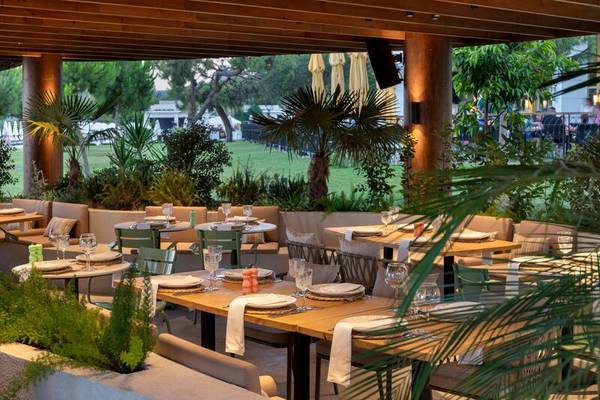 Gartenrestaurant im Sherwood Exclusive Kemer Hotel mit gedeckten Tischen und Pflanzen.