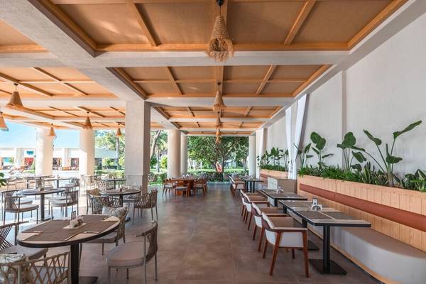 Innenansicht des Restaurants im Sherwood Exclusive Kemer Hotel mit Tischen, Stühlen und Pflanzen.