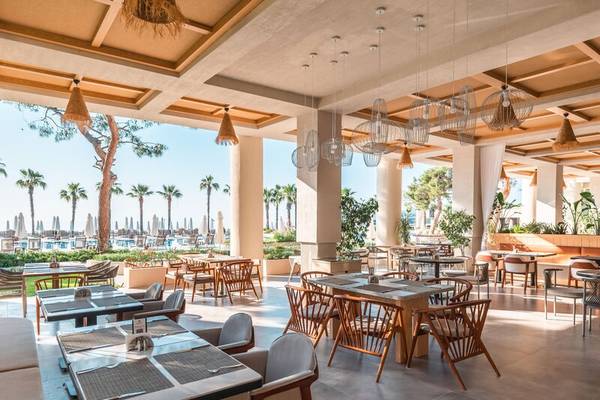 Innenbereich des Sherwood Exclusive Kemer Hotels mit vielen Tischen und Stühlen, umgeben von Pflanzen und Blick auf den Pool.