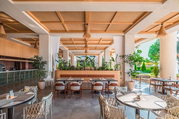 Innenbereich des Sherwood Exclusive Kemer Restaurants mit Tischen, Stühlen und Pflanzen.