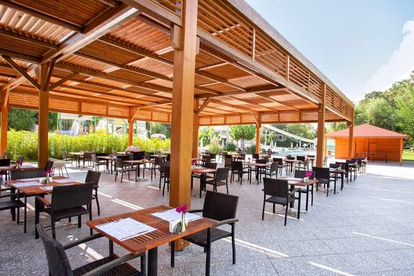 Terrasse des Sherwood Exclusive Kemer Hotels mit Tischen und Stühlen unter einem Holzdach.