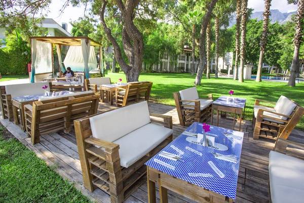 Außenbereich des Sherwood Exclusive Kemer Hotels mit Holzmöbeln, Tischen und Stühlen.