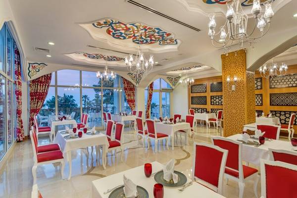 Innenansicht des Restaurants im Sherwood Exclusive Kemer Hotel mit runden Tischen und roten Stühlen.
