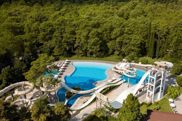 Ein Wasserpark mit mehreren Rutschen und einem großen Pool, umgeben von Bäumen und Liegestühlen.