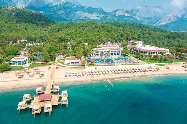 Luftaufnahme des Sherwood Exclusive Kemer Hotels mit Strand, Pool und Bergpanorama.