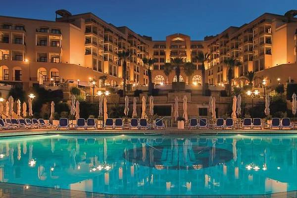 Corinthia St. George's Bay Hotel mit Pool und Lounge-Stühlen bei Nacht
