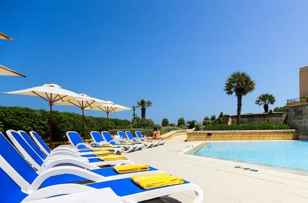 Reihe von blauen und weißen Liegestühlen neben einem Swimmingpool im Corinthia St. George's Bay Hotel
