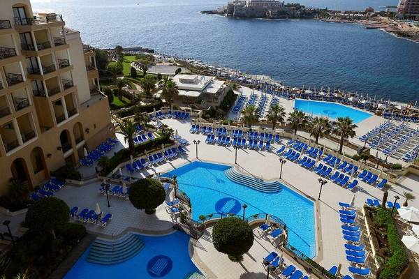 Luftaufnahme des Corinthia St. George's Bay Resorts mit zwei Schwimmbecken und Sonnenliegen am Meer.