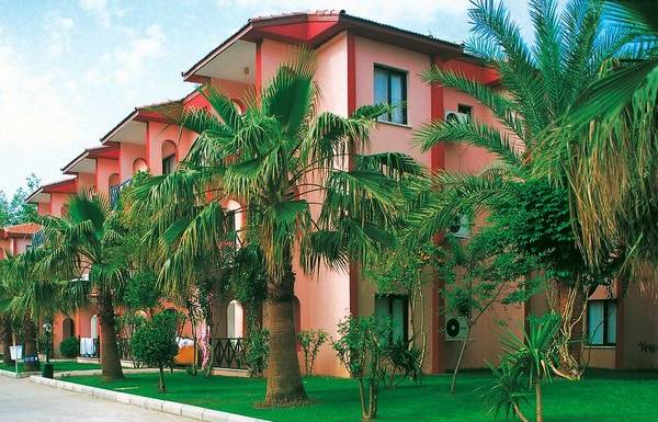 Außenansicht des Süral Garden Hotels mit roten Gebäuden und grünen Palmen.
