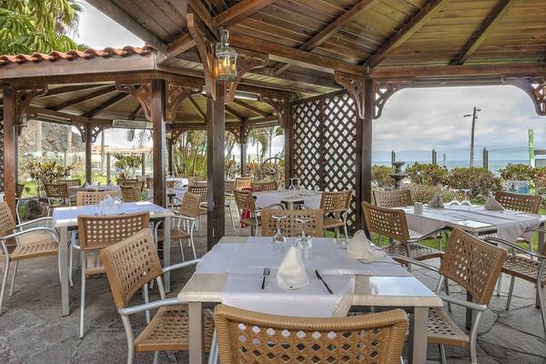 Restaurantterrasse im Hovima Jardin Caleta Hotel mit Tischen und Stühlen unter einem Holzpavillon.