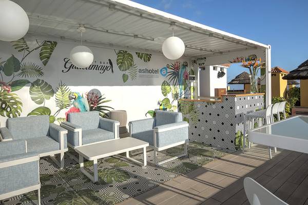 Gartenlounge des Hovima Jardin Caleta Hotels mit blauen Stühlen, Tischen und tropischen Wanddekorationen.