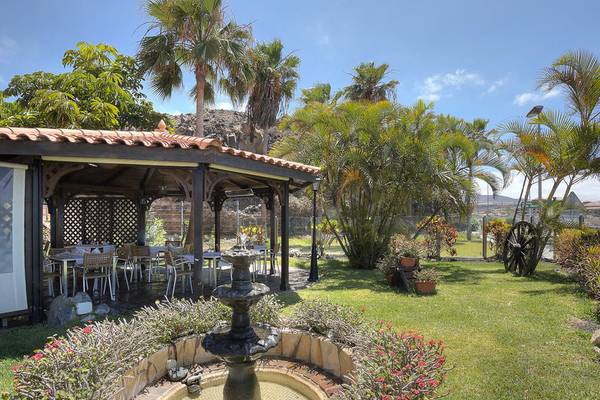 Außenbereich des Hovima Jardin Caleta Hotels mit Pavillon, Tischen und Stühlen, umgeben von Pflanzen und Bäumen.