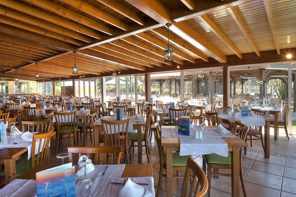 Innenansicht des Restaurants im Hovima Jardin Caleta Hotel mit Holztischen und Stühlen, gedeckten Tischen und Deckenlampen.