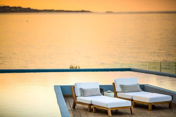 Zwei weiße Liegestühle auf der Dachterrasse des Abaton Island Resort & Spa mit Blick auf den Pool und den Ozean