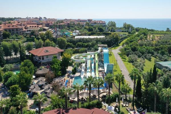 Luftaufnahme des Club Grand Side Wasserparks mit Rutschen und Pool, umgeben von Bäumen und Blick auf das Meer.